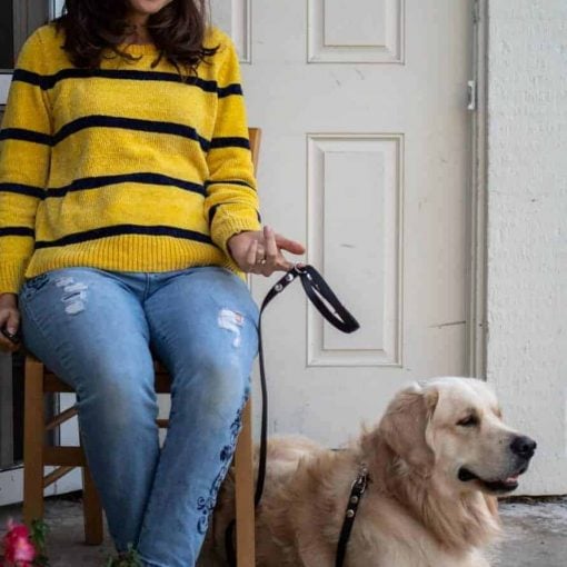 Woman wearing a striped yellow and black shirt sitting with golden retriever with a black leash.